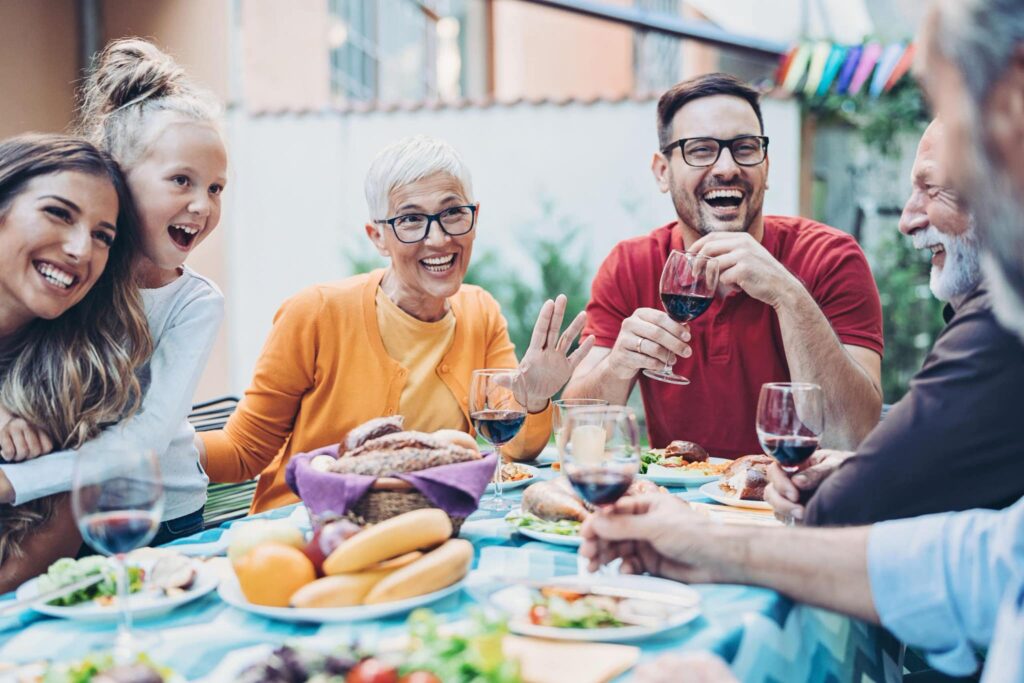 A group on a patio laughs and clinks glasses of red wine, surrounded by dishes and colorful decorations, creating a festive atmosphere.