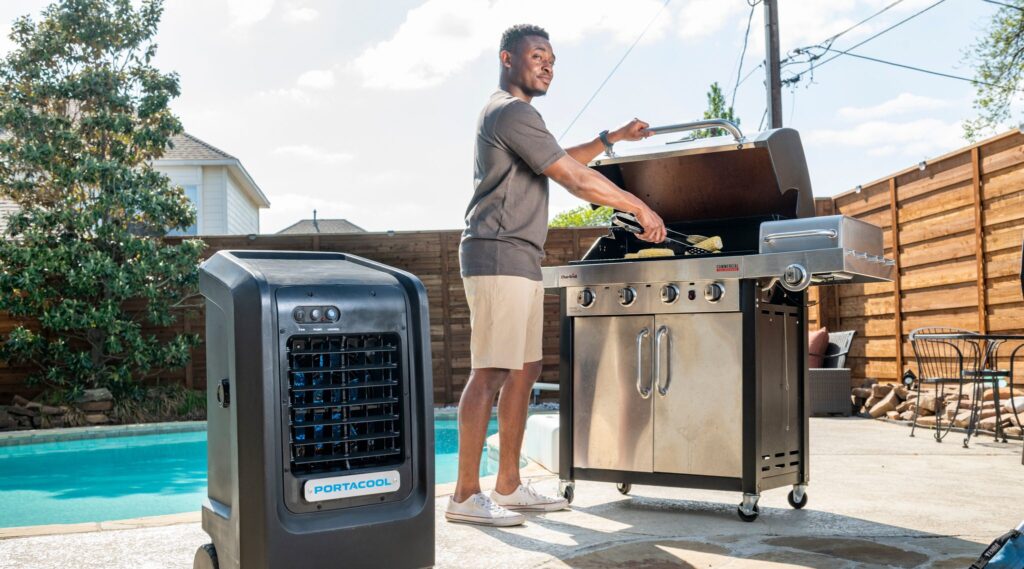 Man grills by the pool knowing his guests are enjoying themselves in the cool breeze and cooled zone created by the air cooler.