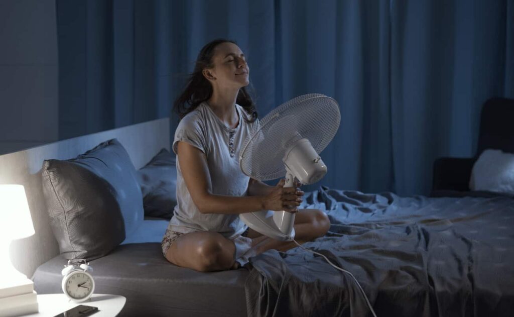 A woman sits cross-legged on a bed, wondering Are swamp coolers better than fans?