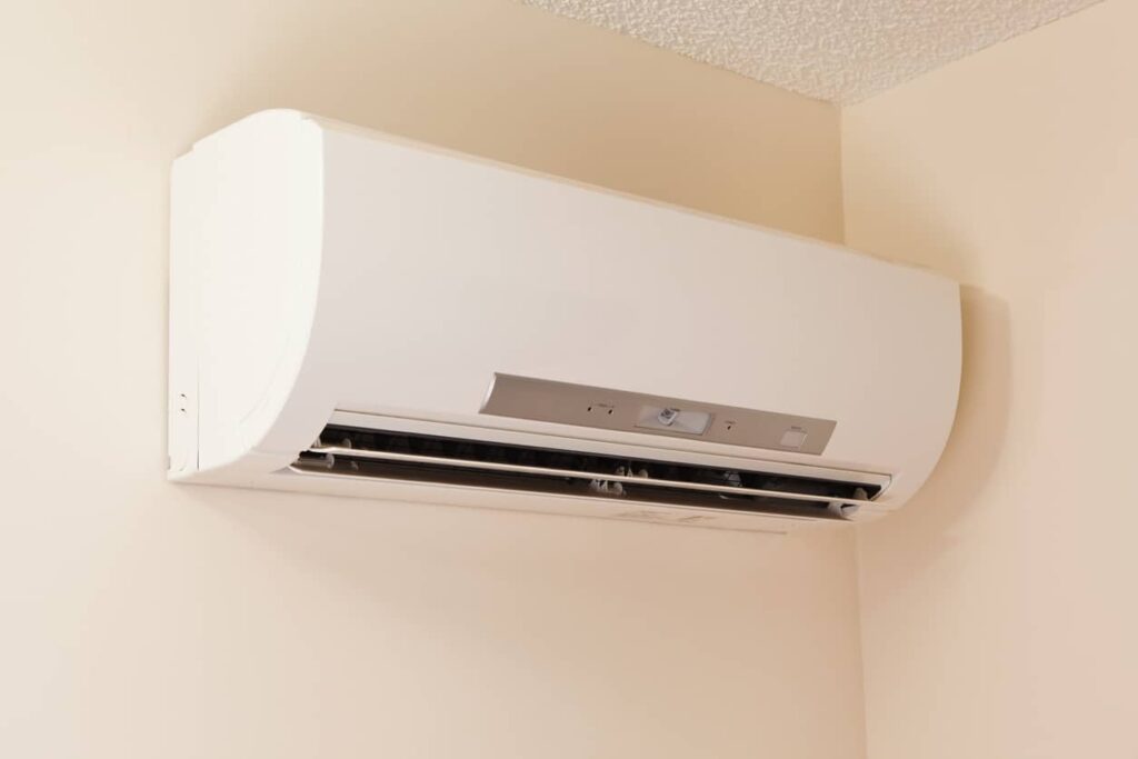 A white wall-mounted ductless unit with an open front panel, revealing vents and controls, is installed in a room corner with beige walls.