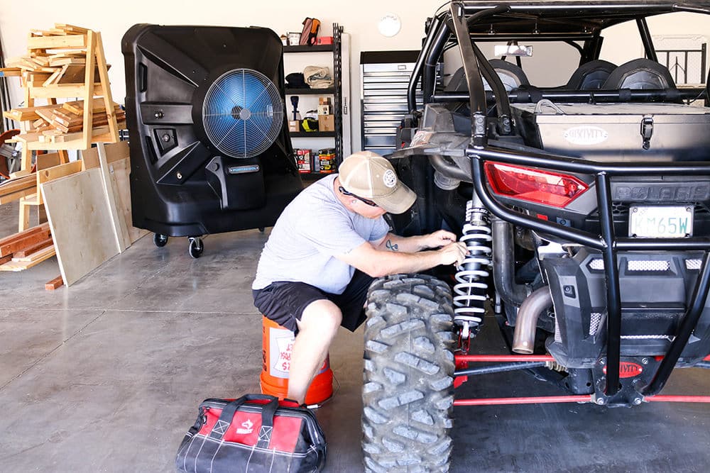 Man works on his side by side in his garage at Addicted to DIY, which is cooled by a larger evaporative cooler from the Portacool lineup.