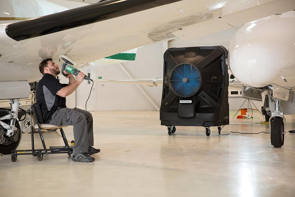 Employee works on an airplane wing in front of an Apex swamp cooler, which is making the hanger comfortable all summer long.