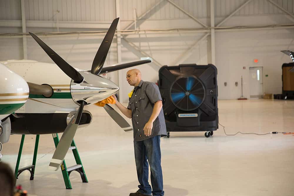 Curtis Airfield worker in front of a Portacool portable evaporative cooler, polishing an airplane propeller.