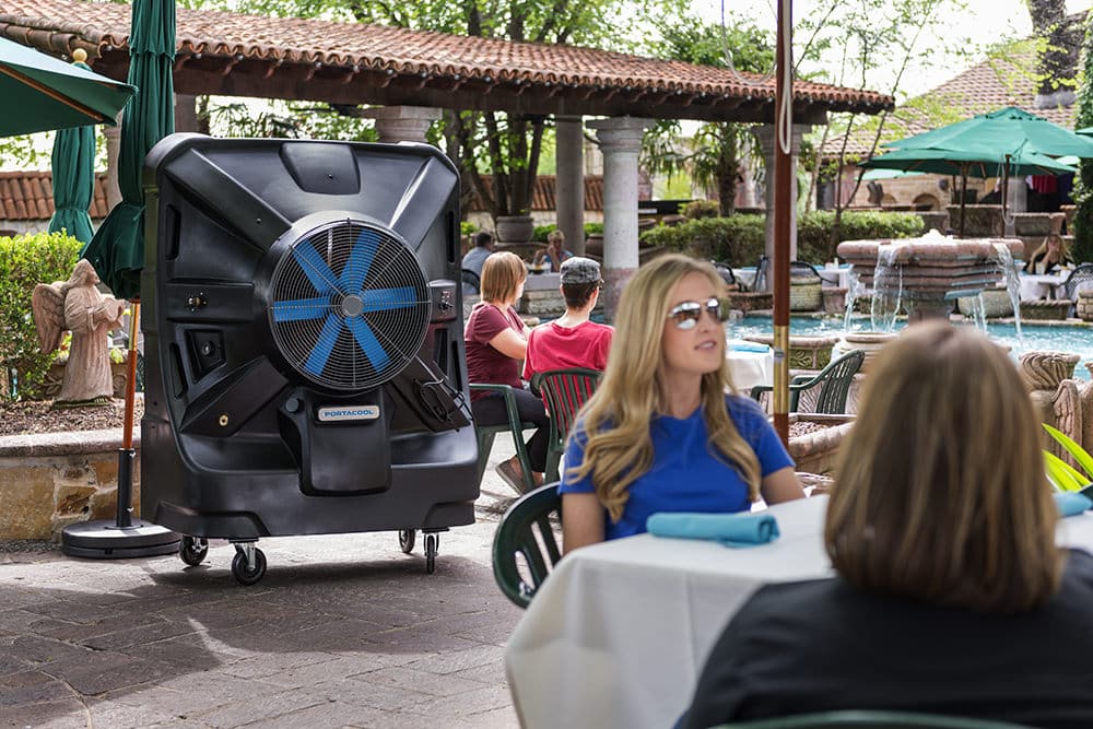 Outdoor dining at Joe T. Garcia's in Fort Worth, with guests enjoying meals by the pool under shaded tables and a large portable cooler enhancing comfort.