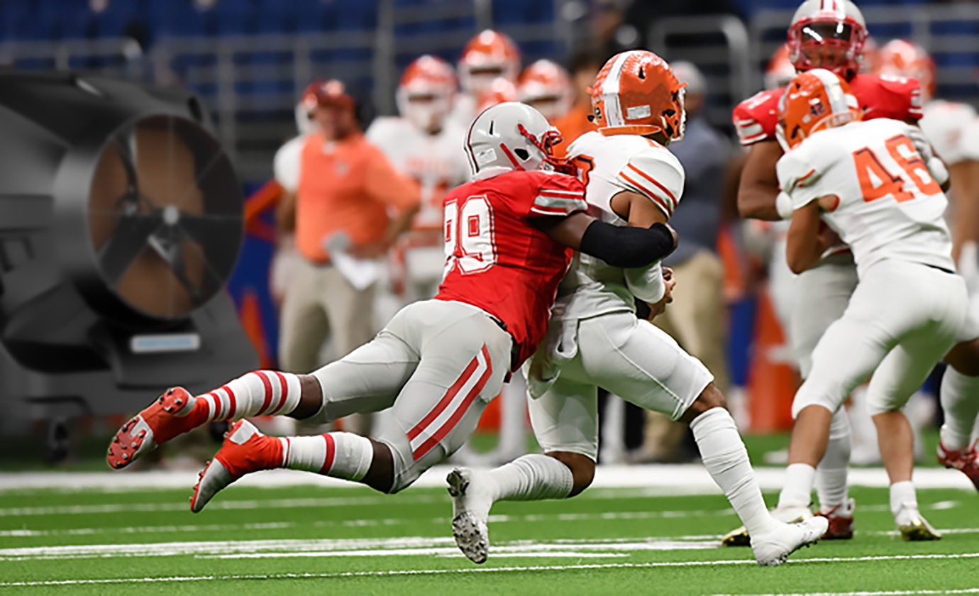 Football players engage in full-contact sport near a powerful air cooler on the sideline.