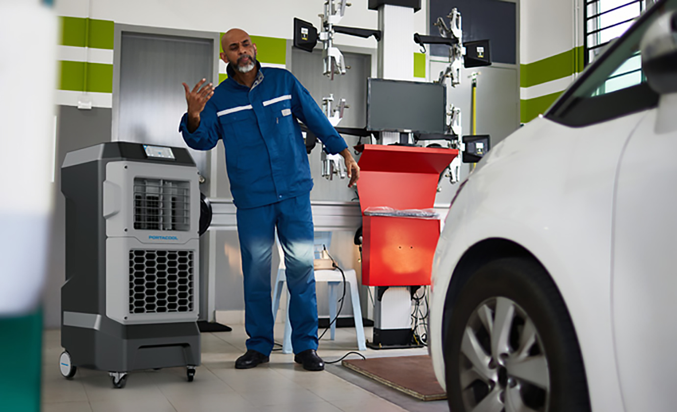 Mechanic in large garage works on cars in cool comfort that traditional A/C can't afford such open spaces.