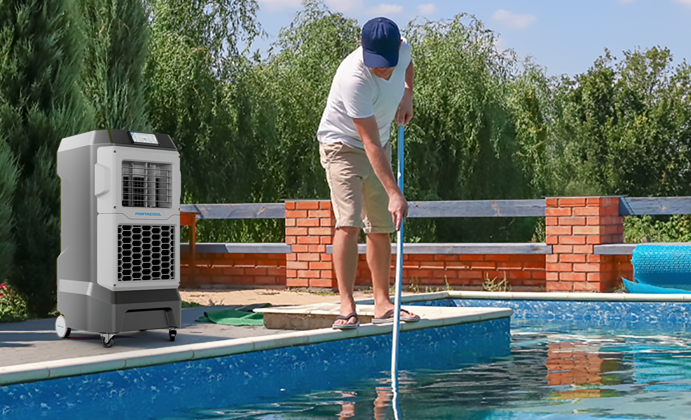 Person in white shirt, shorts, and cap cleans pool with long pole. Nearby is a portable cooler. Green trees and brick wall create inviting ambiance.