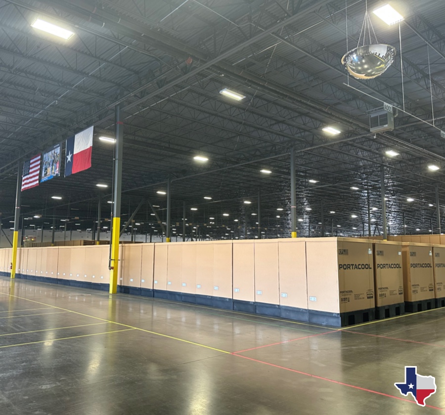 Warehouse interior with stacked "PORTACOOL" boxes, high ceilings, American and Texas flags overhead, and a Texas emblem in the corner.